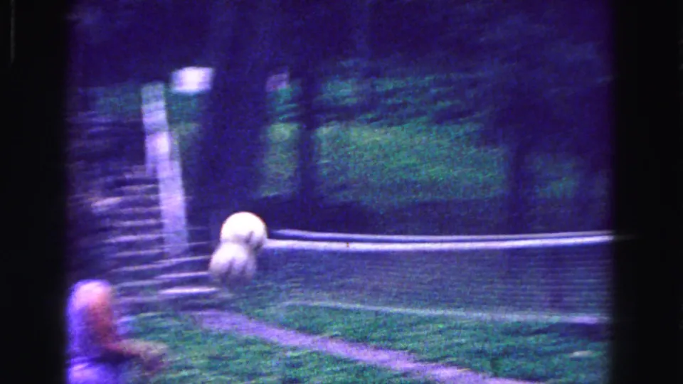 A ball travels across the frame near the net while a player moves through the blurred foreground in this 1967 backyard volleyball shot.
