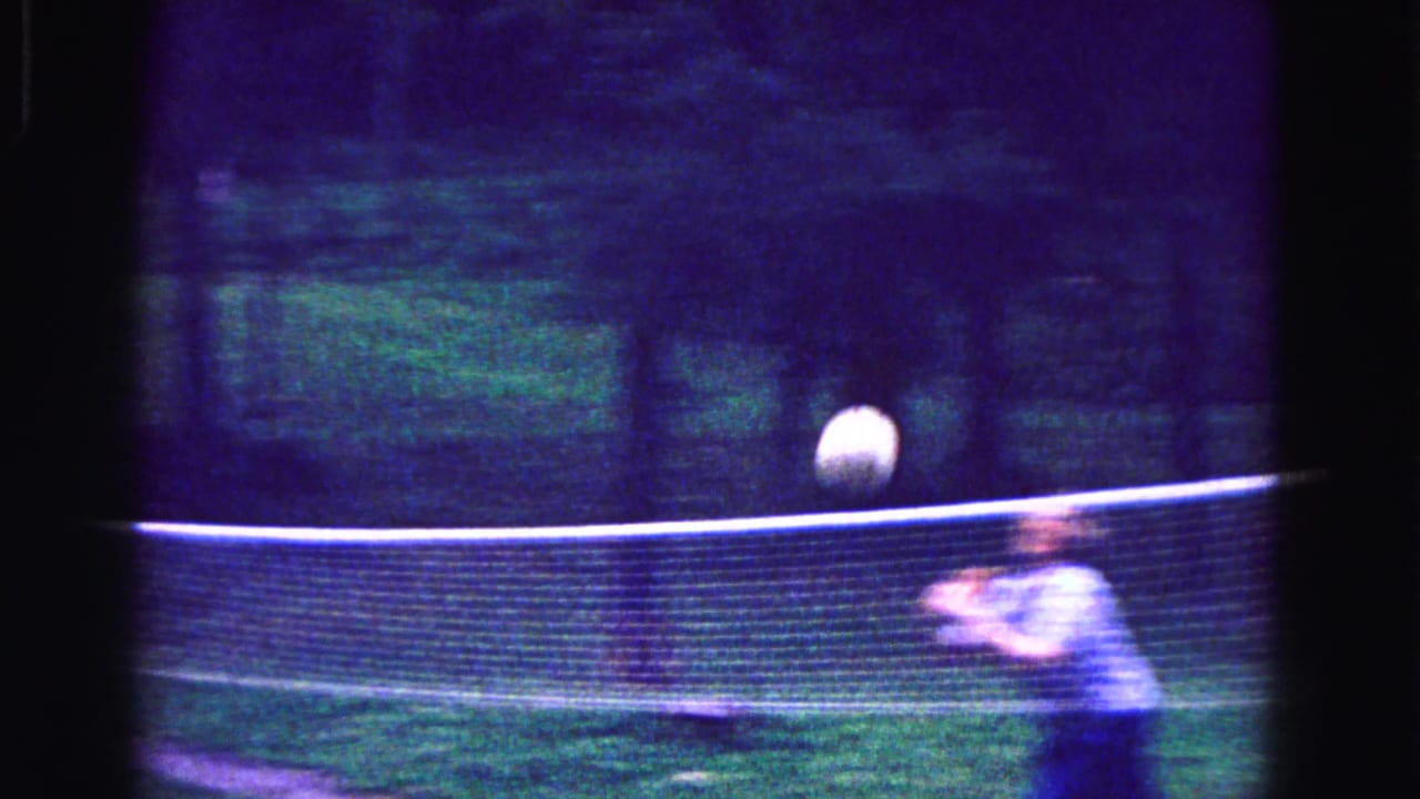 Woman reaches toward a volleyball near a portable net on a grassy lawn.