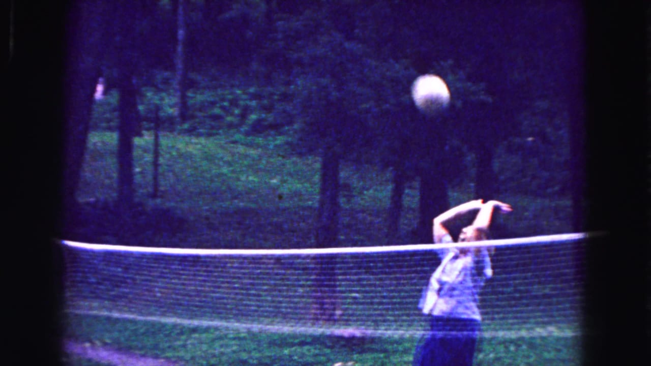 A woman in a light sleeveless dress plays volleyball beside a net in this 1967 Galena, Illinois home-movie frame.