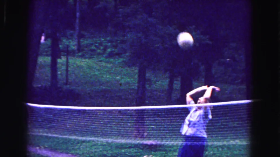 A woman in a light sleeveless dress plays volleyball beside a net in this 1967 Galena, Illinois home-movie frame.