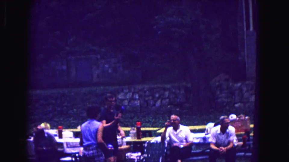 Adults sit and stand near picnic tables in shaded outdoor 1967 family-reunion footage from Galena, Illinois.