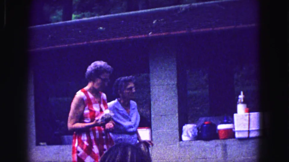 At the Galena gathering, the women appear to talk beside a shelter wall while coolers and supplies sit nearby.