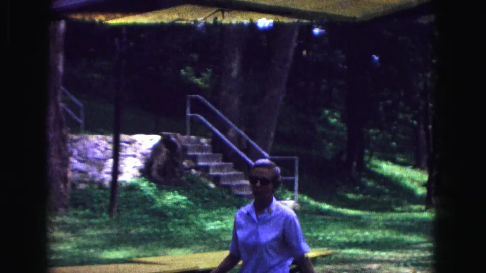 In Galena, Illinois, a woman in glasses walks through a wooded park area near stone steps and a metal railing in 1967 home-movie footage.