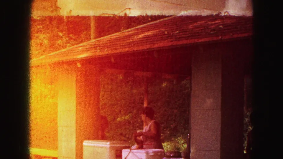 A strong yellow-orange film wash partially obscures a shelter or pavilion area with a woman near picnic tables and columns.