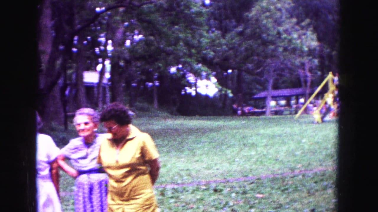 Older women stand together on a grassy lawn with trees and a swing set behind them.