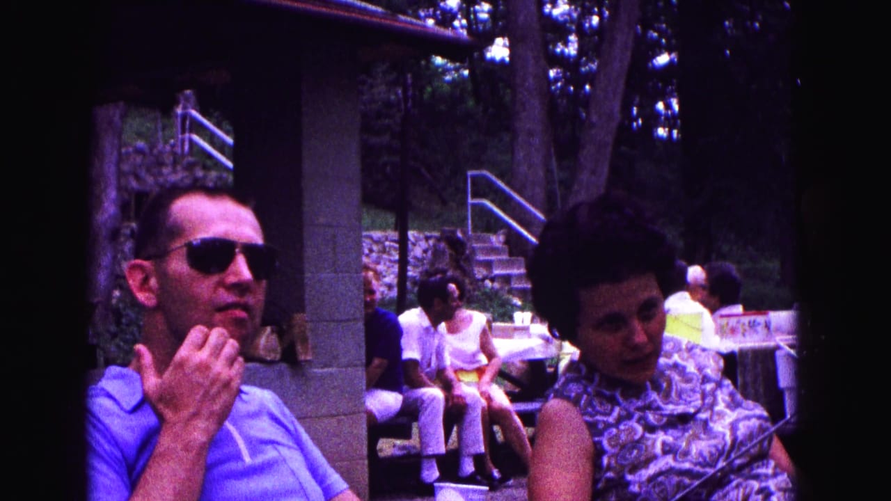 In this 1967 Galena, Illinois home-movie frame, a man in sunglasses and a woman in a patterned dress sit near a pavilion and picnic area.