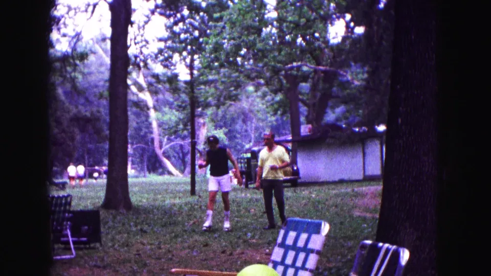 Two men stand on a grassy park area in Galena, Illinois, with lawn chairs, trees, and a small structure visible nearby.