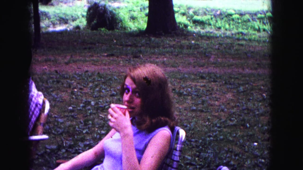 In Galena, Illinois home-movie footage dated 1967, a young woman sits in a lawn chair holding a red cup under trees.