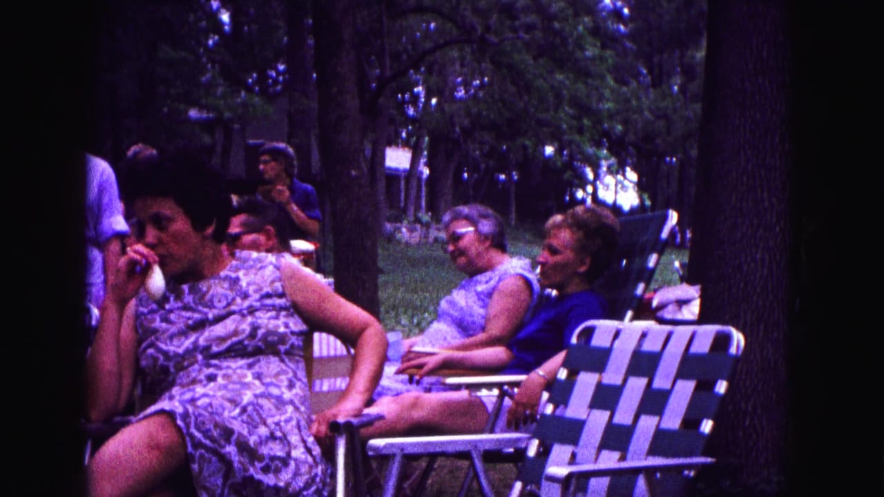 A group of women sits outdoors in striped lawn chairs beneath trees in 1967 Galena, Illinois footage.