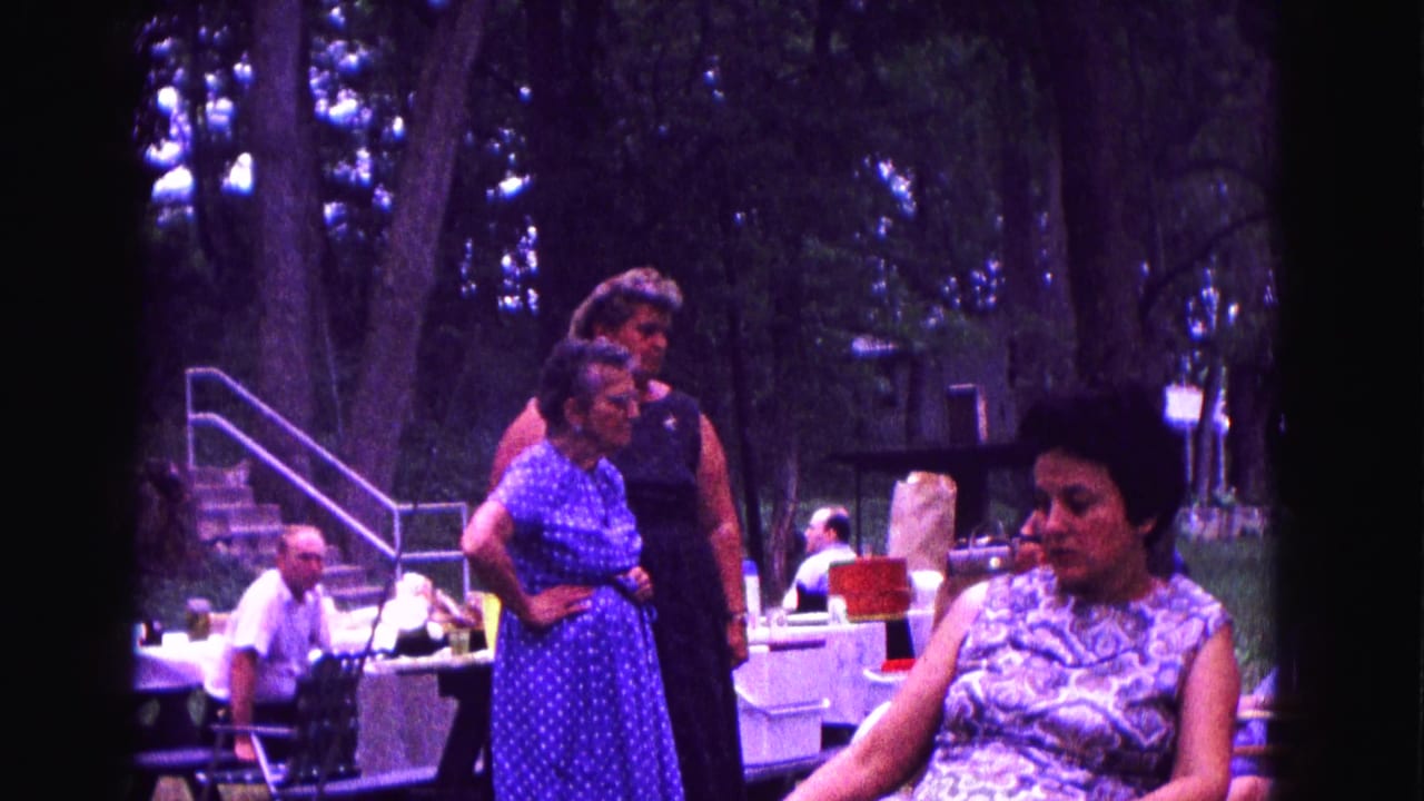 1967 Galena, Illinois home-movie frame showing women in 1960s dresses near picnic tables under trees.