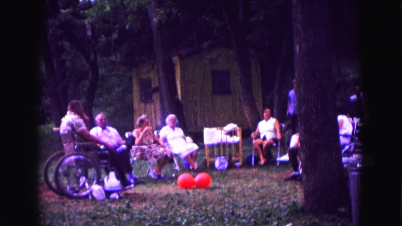 Adults relax in a wooded Galena backyard, with red balloons on the grass and a rustic shed behind them.