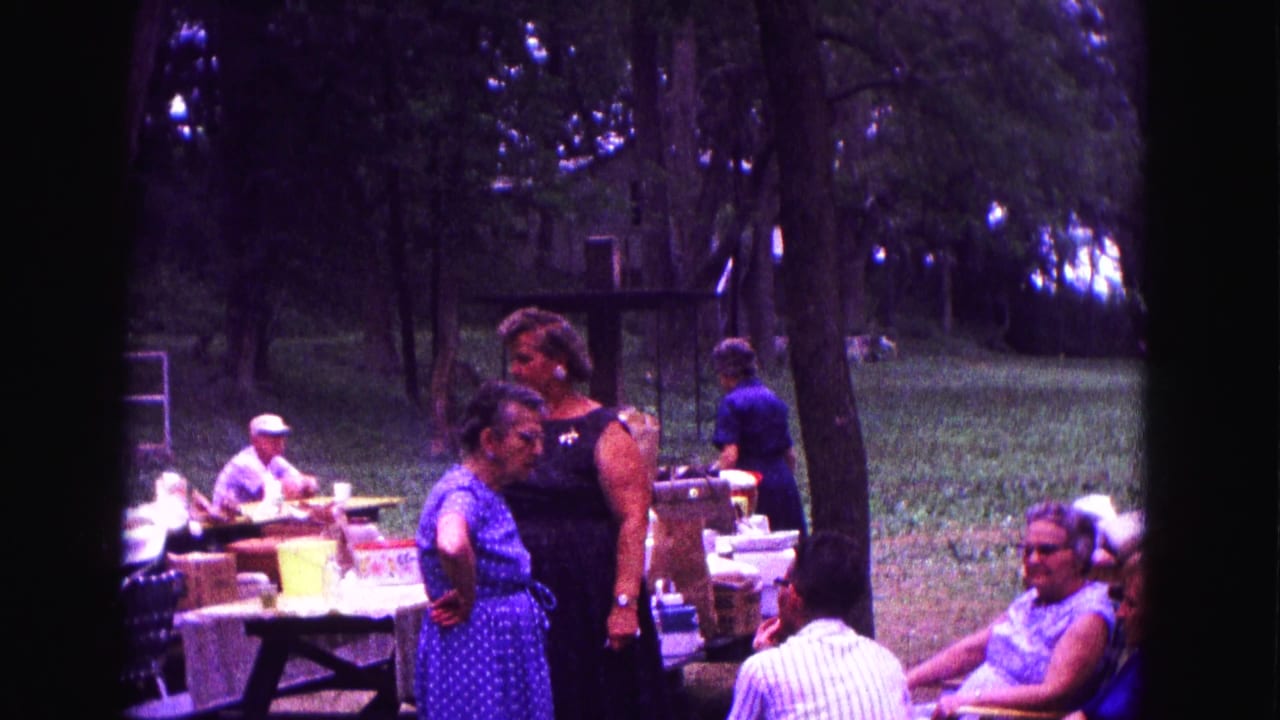Women stand beside picnic tables while adults sit nearby.