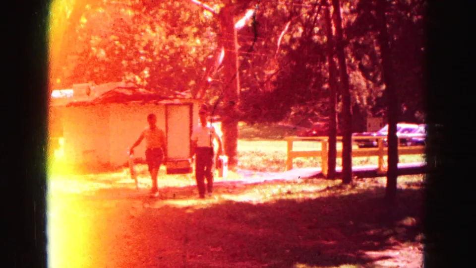 Two men in the Galena park footage walk toward a picnic area carrying coolers, with trees, fence, cars, and strong film flare visible.
