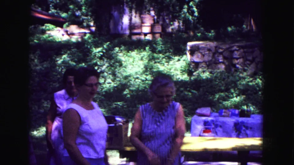 1967 Galena, Illinois home-movie frame with women near a picnic table, surrounded by trees, grass, and stone or masonry landscaping.