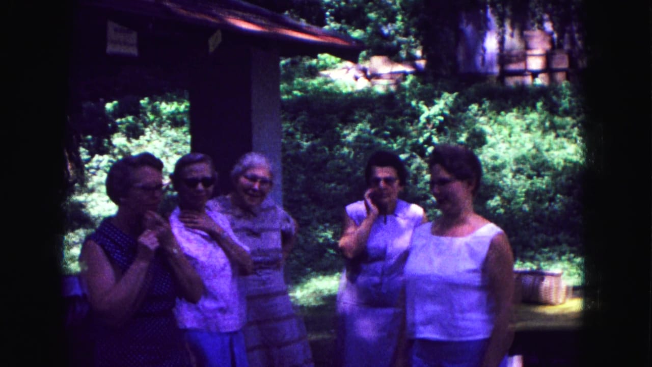Women converse on a covered porch in Galena, Illinois, with summer clothing and foliage visible in the 1967 8mm frame.