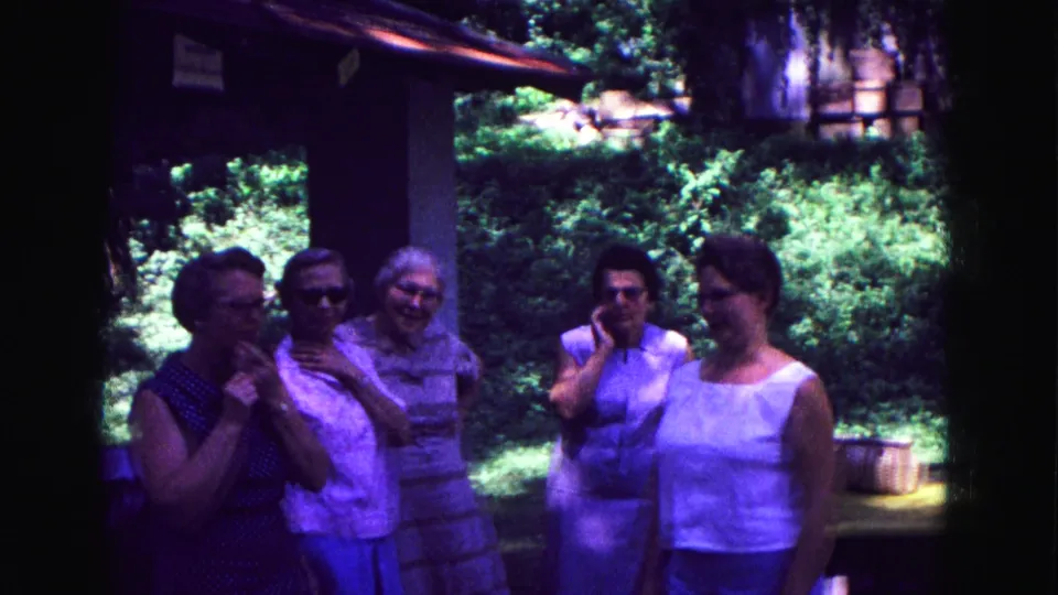 Women converse on a covered porch in Galena, Illinois, with summer clothing and foliage visible in the 1967 8mm frame.