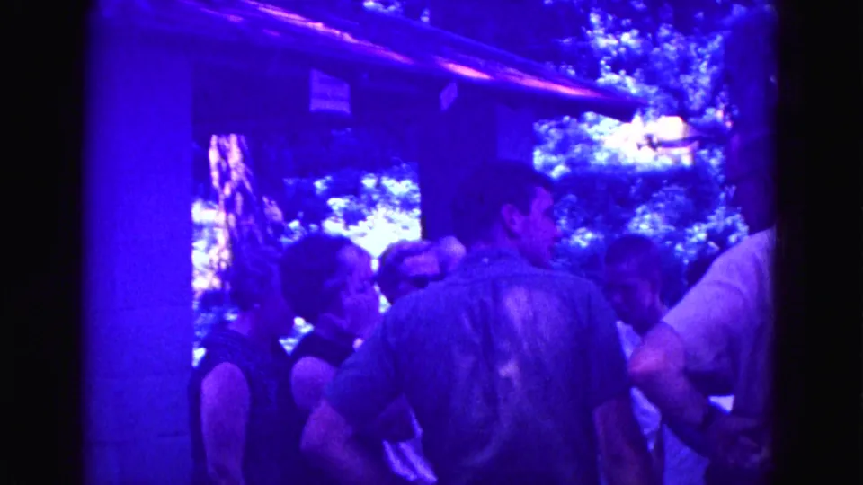 Adults gather closely under the porch in a heavily blue-shifted 8mm frame from the Galena home-movie clip.