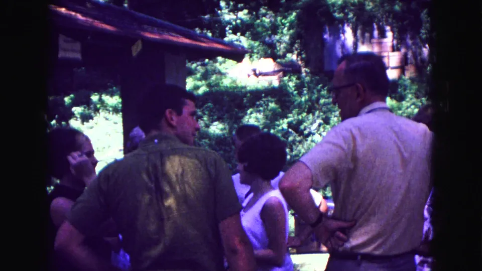 Men and women stand near the shaded porch edge in the 1967 Galena scene, with bright trees behind them.
