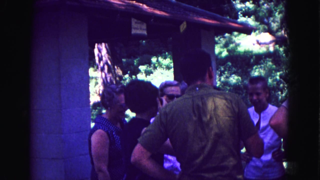 Adults gather under a small outdoor shelter surrounded by trees.