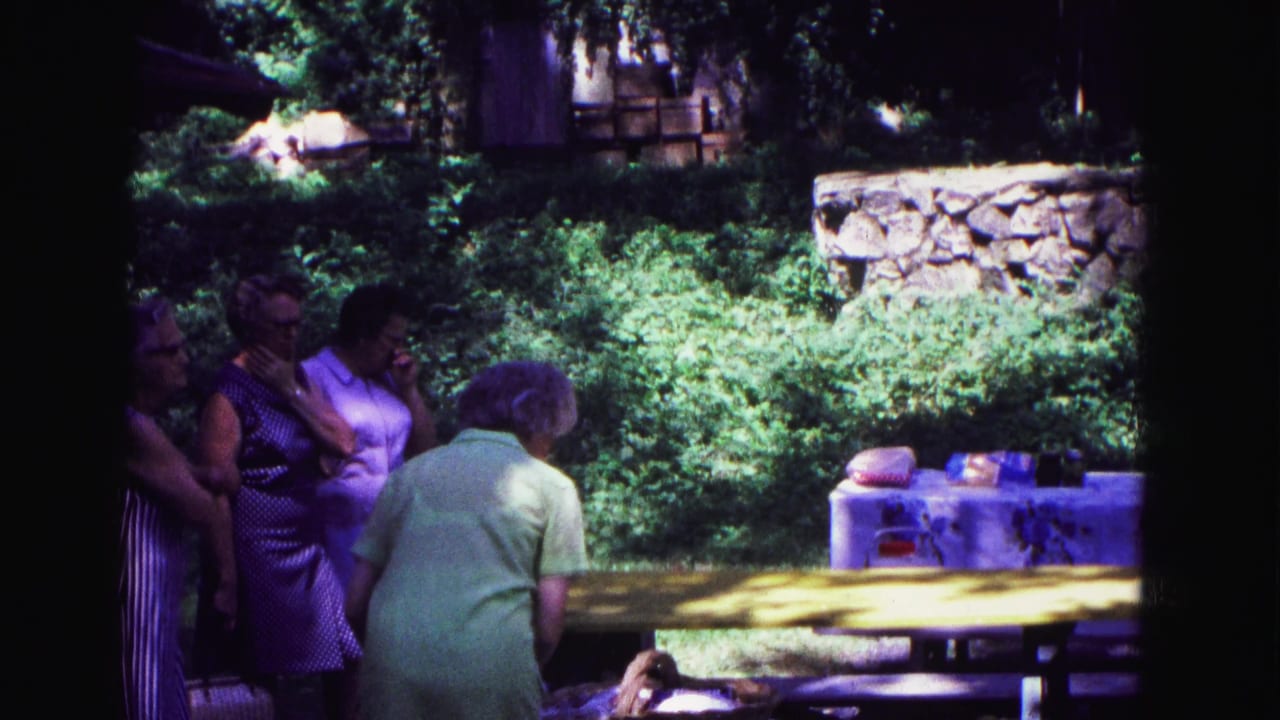 Women beside picnic tables with greenery and a stone wall behind them.
