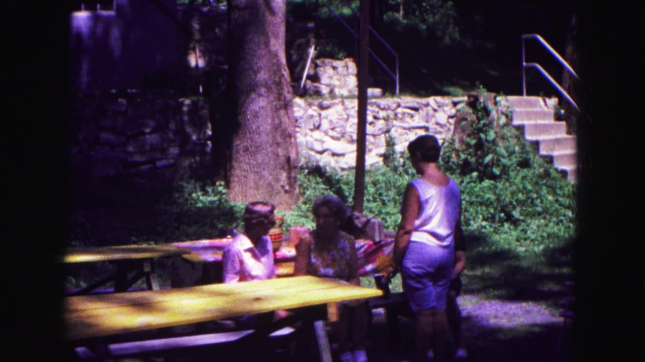 Adults gathered at a yellow picnic table in a shaded outdoor area.