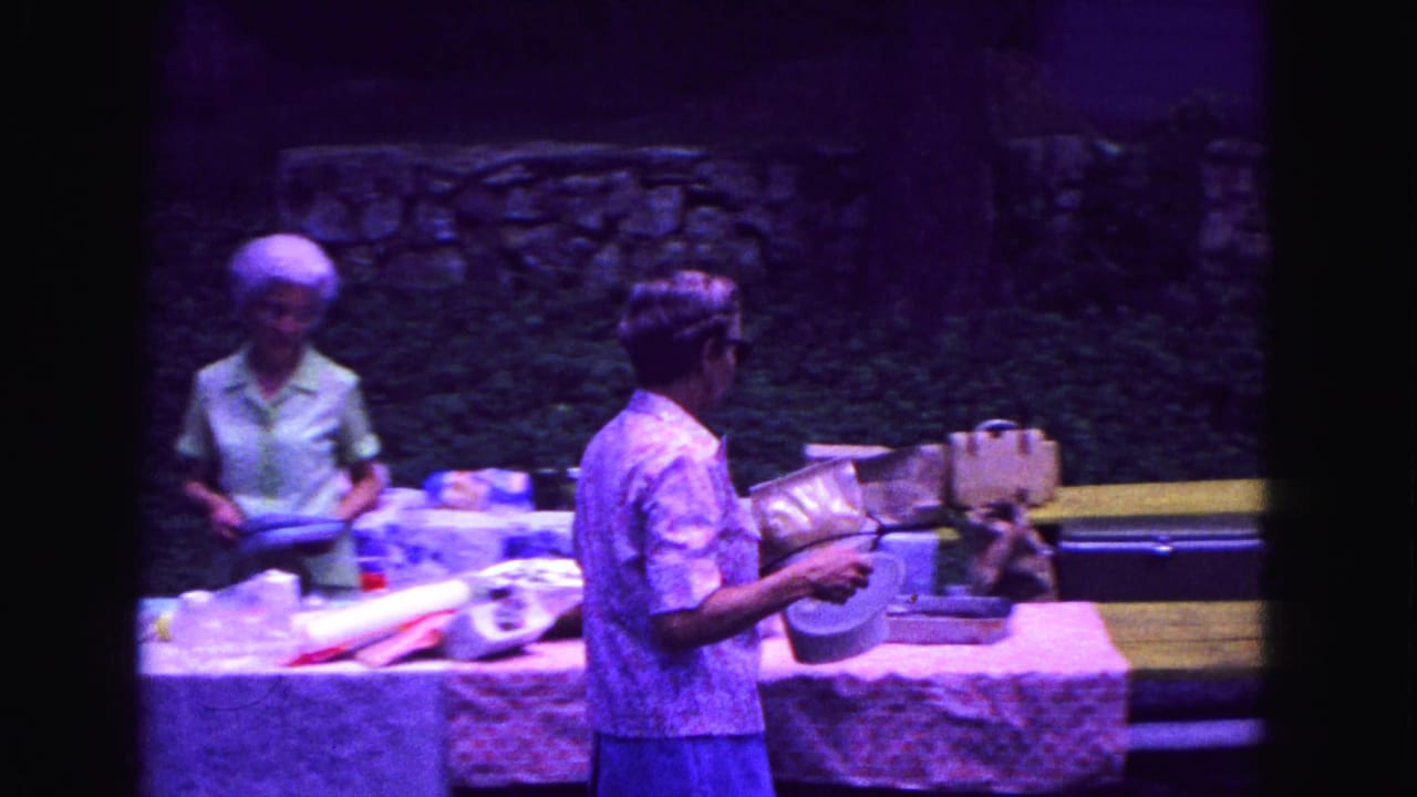 Two women at a picnic table with dishes and food containers outdoors.
