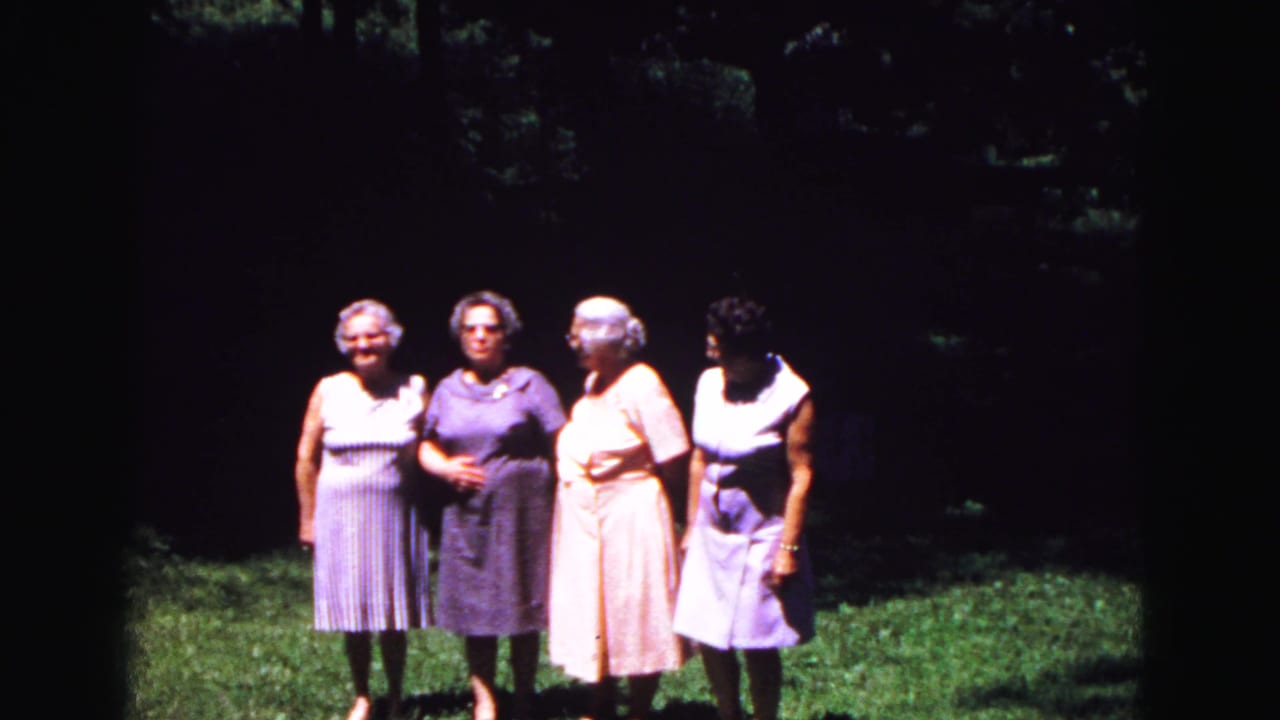 Four older women in striped, purple, peach, and lavender dresses pose together outdoors in the 1967 Galena, Illinois home movie.