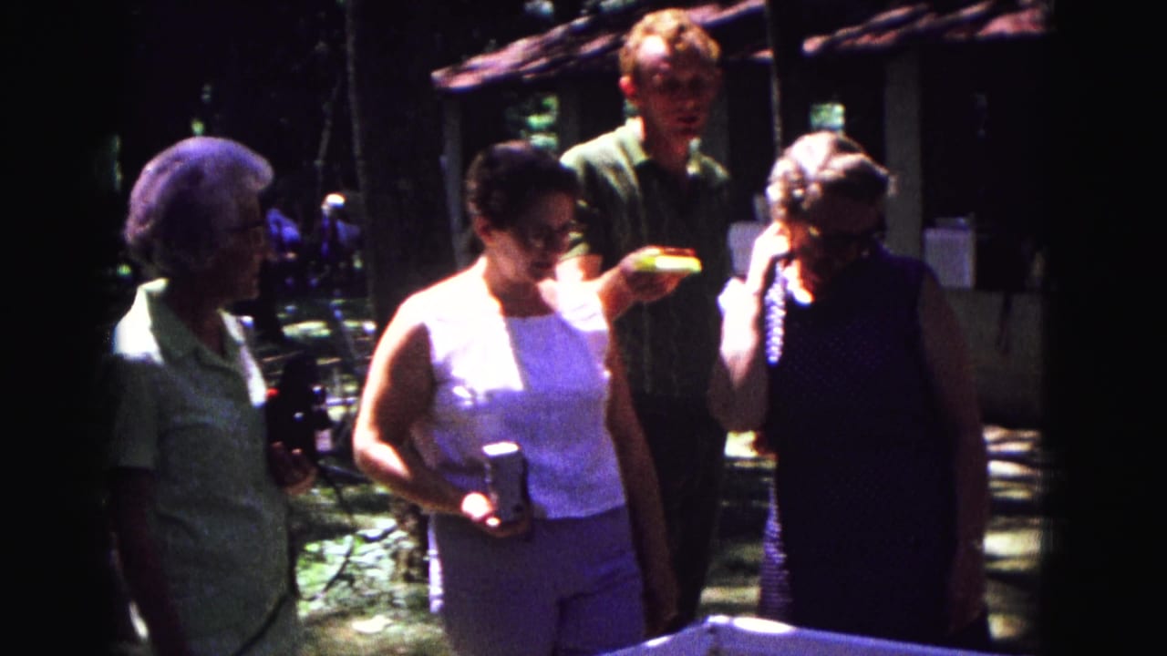 Adults walk and talk near a rustic building while holding drinks and food.