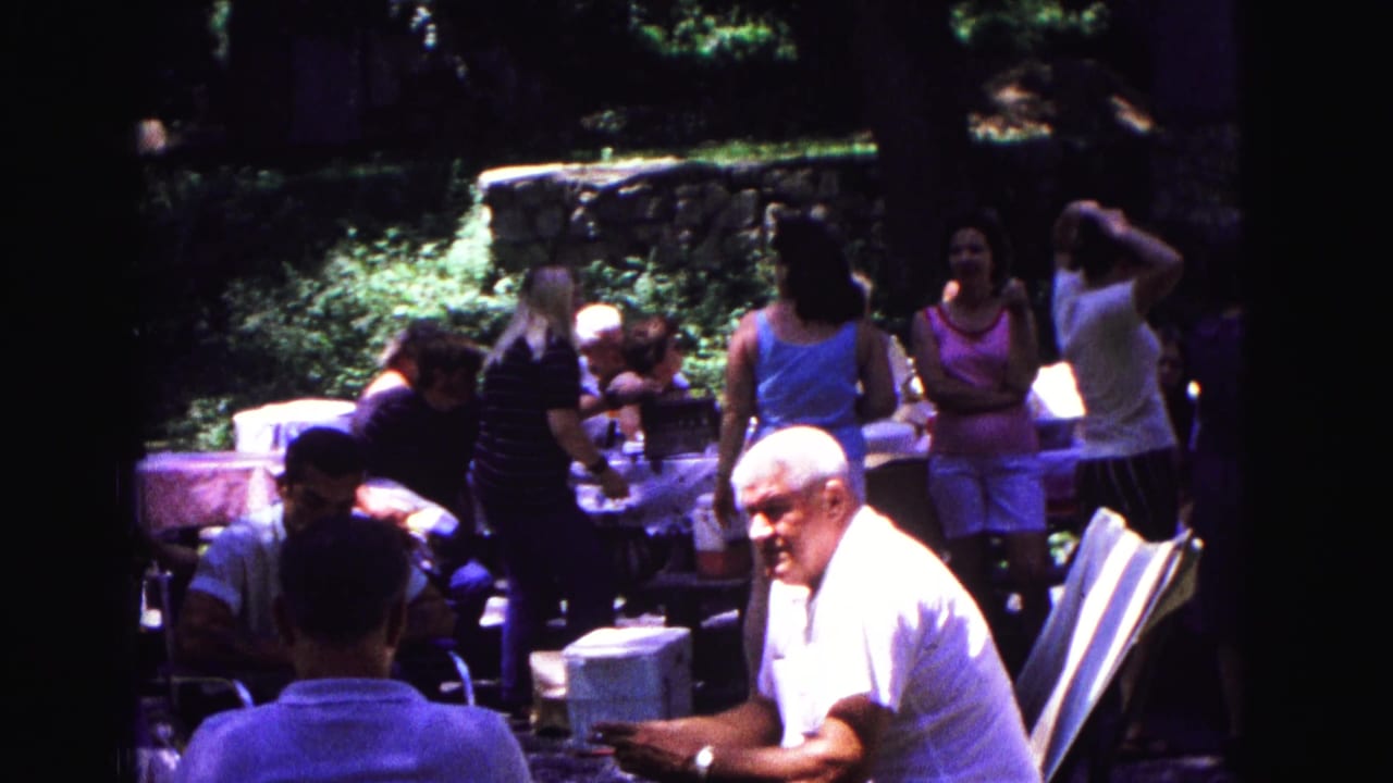 Adults at a 1967 backyard gathering in Galena, Illinois, with tables, chairs, trees, and a stone wall visible.
