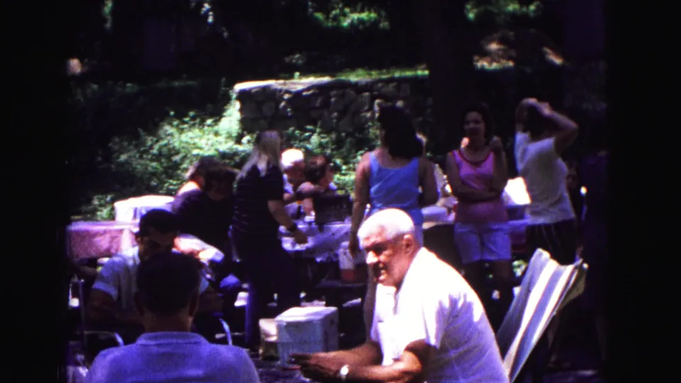 Adults at a 1967 backyard gathering in Galena, Illinois, with tables, chairs, trees, and a stone wall visible.