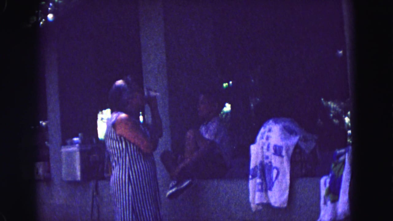 Woman in a striped dress stands near a pillar at a dim nighttime gathering.