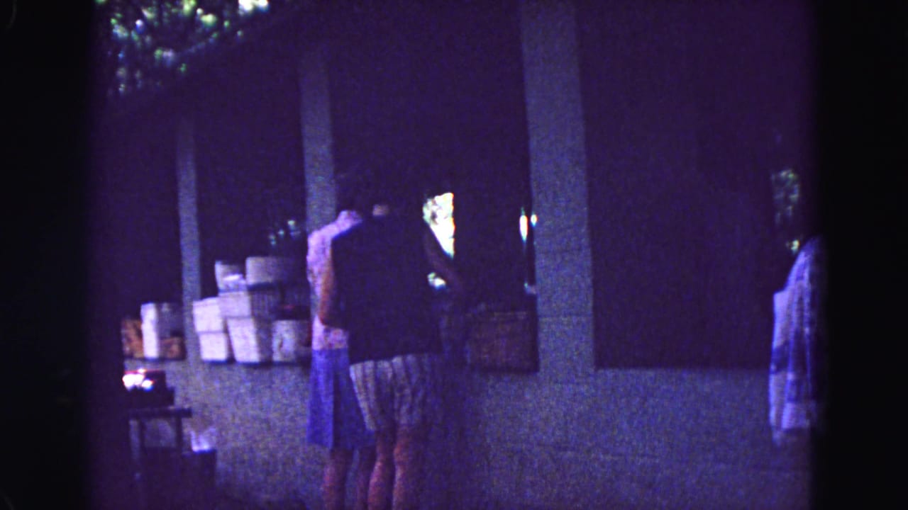 1967 Galena, Illinois home-movie frame showing women at a covered outdoor counter beside stacked boxes.