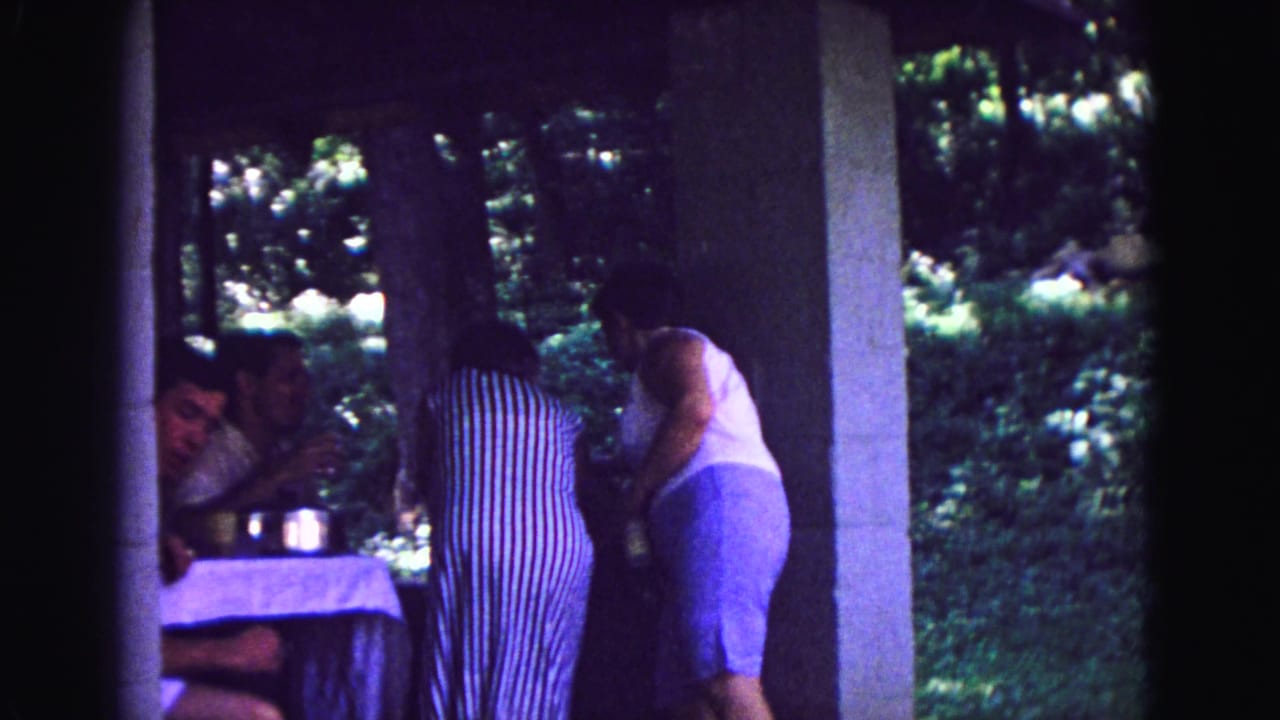 Two women bend over a patio table as two seated people are partly visible at left.