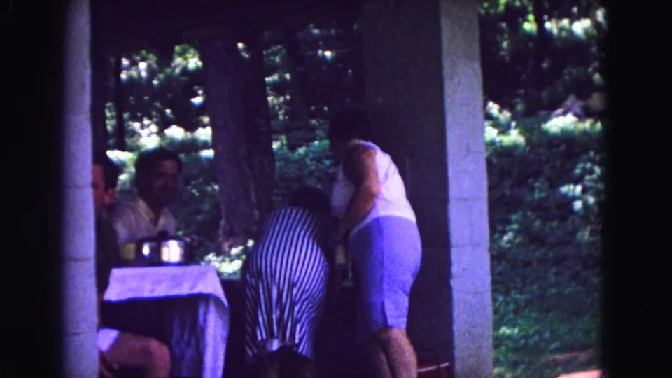 1967 Galena, Illinois home-movie frame showing adults near a pavilion table under trees, with one person bending near the table.