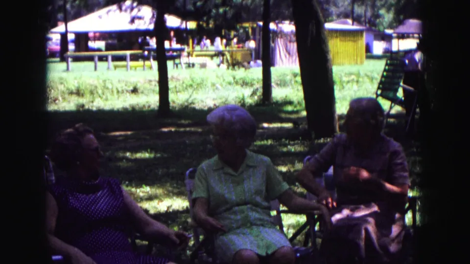 1967 Galena, Illinois home-movie still of three older women conversing in lawn chairs near a picnic area.
