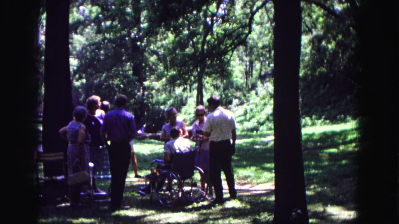 Home-movie frame from Galena, Illinois in 1967 showing a small group conversing outdoors beside a wheelchair.