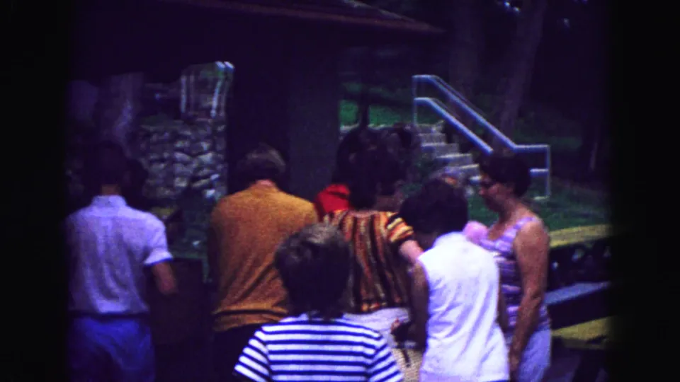 A late moment in the 1967 Galena home movie shows adults gathered by cabin stairs, with dusk shadows and visible 8mm grain.