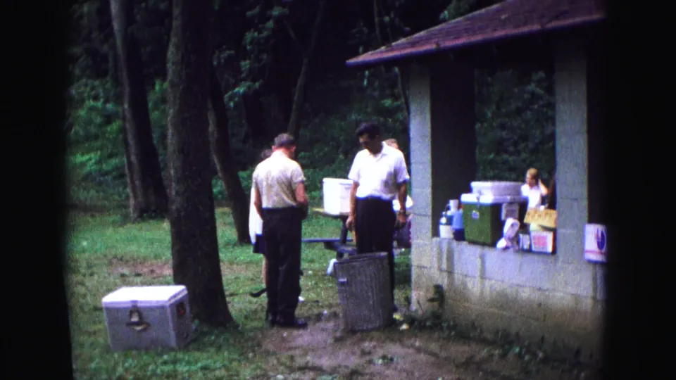 1967 Galena, Illinois park picnic frame with adults, coolers, boxes, a dog, trees, and an open pavilion.