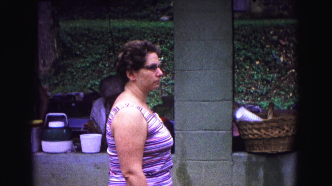 Woman in a striped tank top stands in profile beside picnic supplies under a shelter.