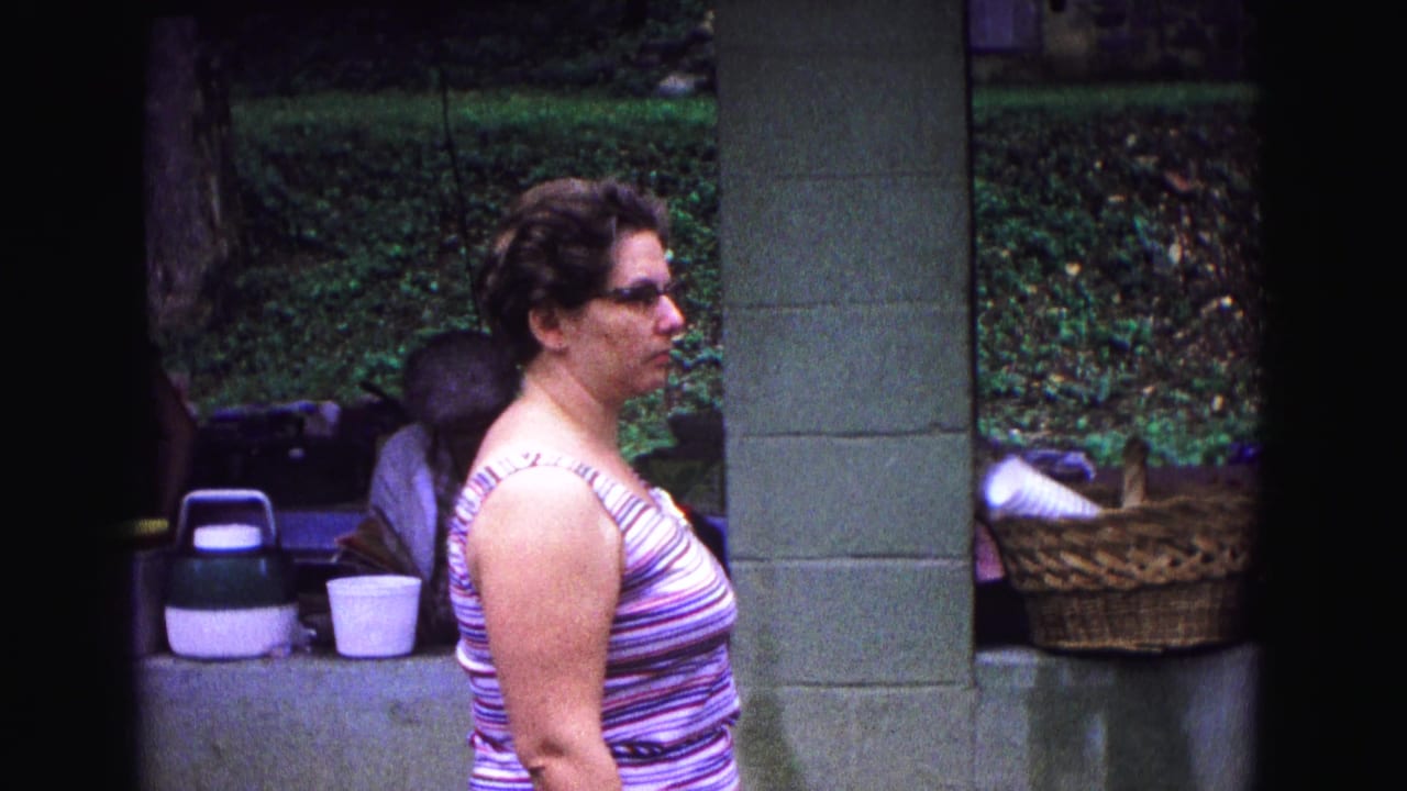 Woman in striped tank top stands near a concrete post with picnic items behind her.