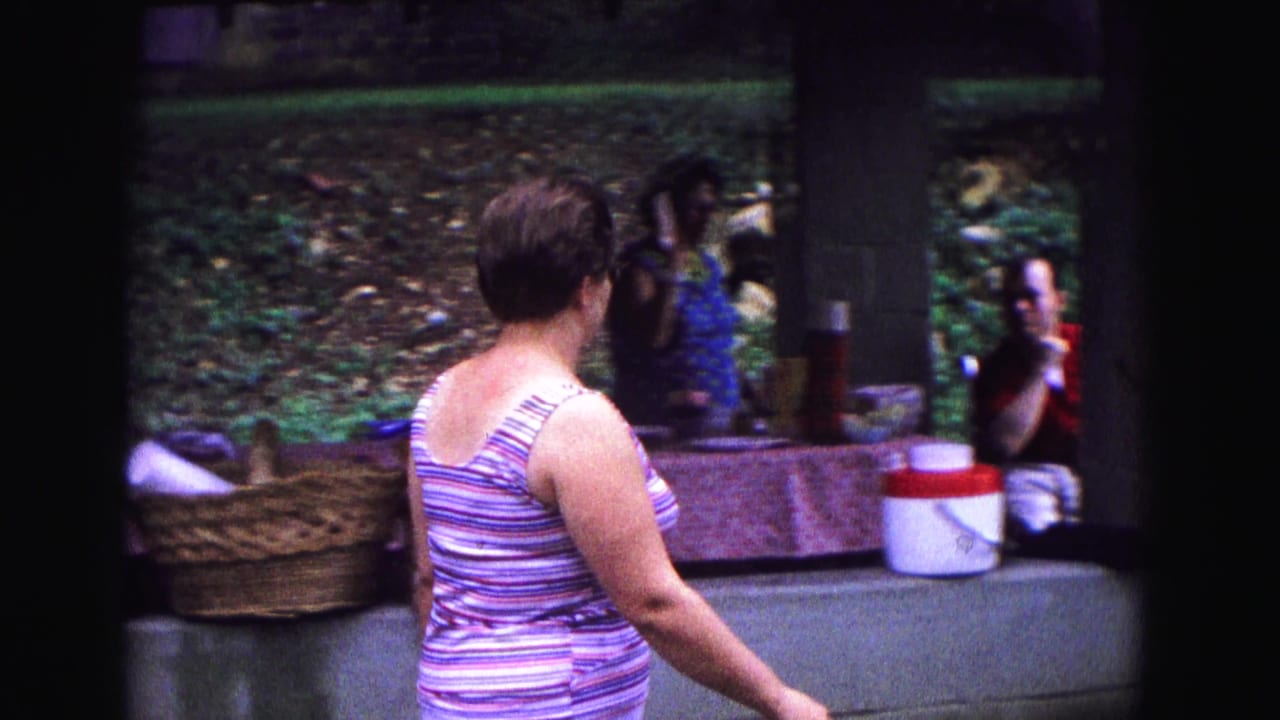 Woman in a striped tank top walks inside a park pavilion near baskets and picnic items.