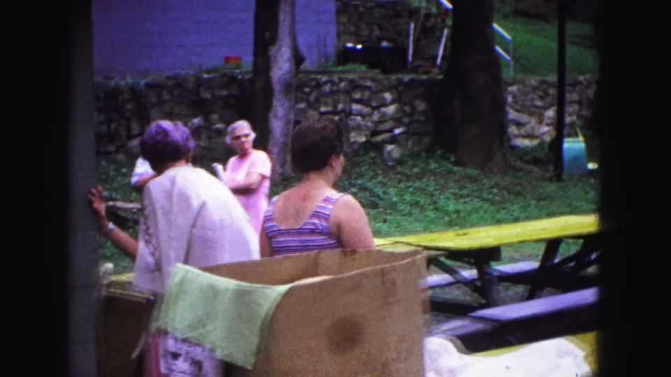 Adults stand and talk near a Galena park pavilion, with a picnic table and stone wall visible behind them.