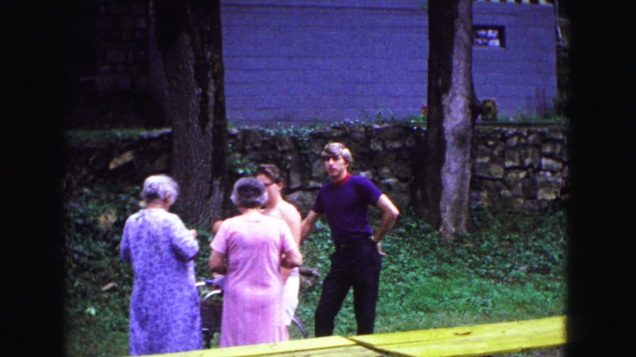 Four adults stand in a grassy backyard near trees and a stone wall.