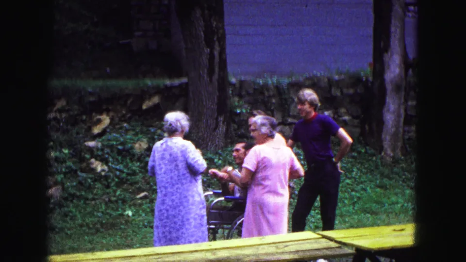 In the 1967 backyard footage, two women face away as other adults remain partly visible near grass, trees, and a stone wall.