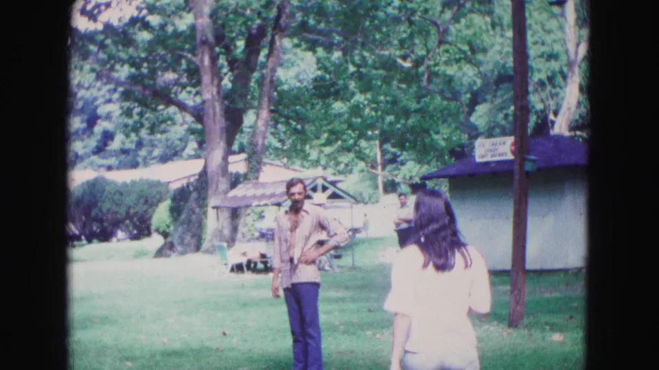 1967 Galena, Illinois park frame with a woman viewed from behind and a man near a refreshment kiosk.