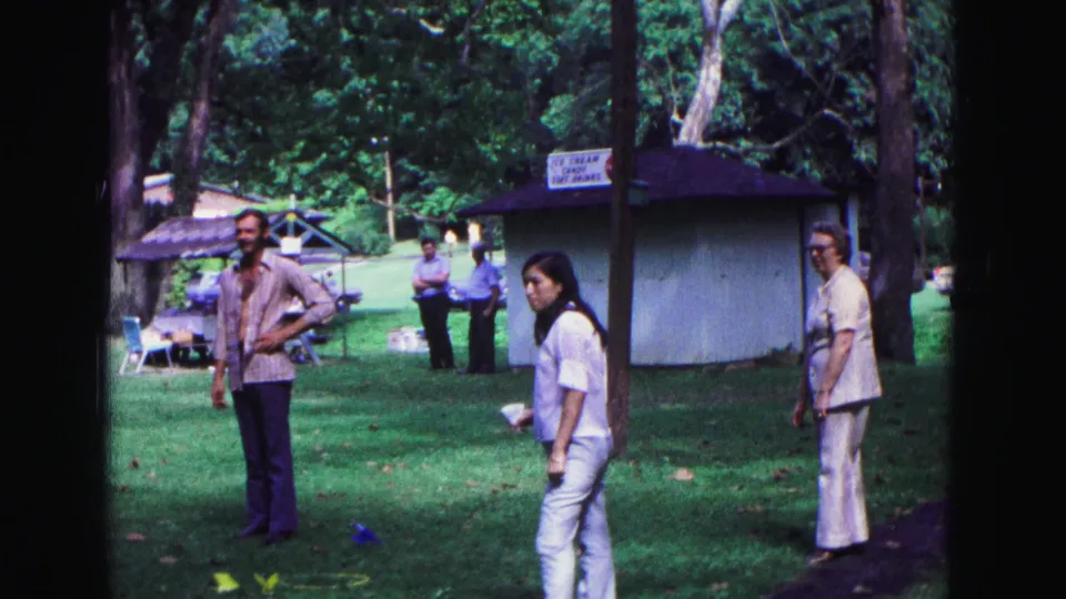 At the 1967 Galena park event, a woman in white pauses near colored lawn markers as other adults watch nearby.