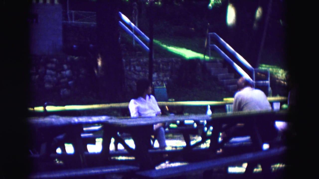 1967 Galena, Illinois frame showing adults at an outdoor picnic table, partially obscured by dark 8mm frame edges and low light.