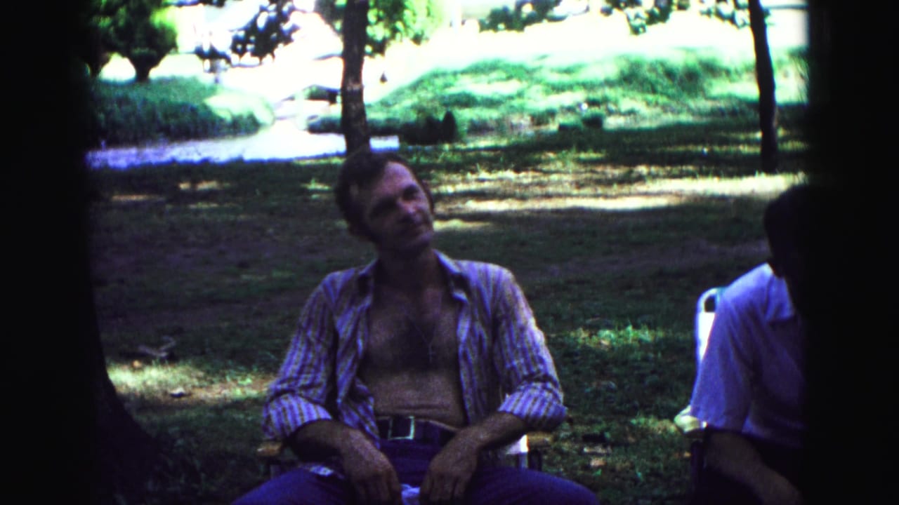 Seated man looks upward while another adult is partly visible at the right edge.
