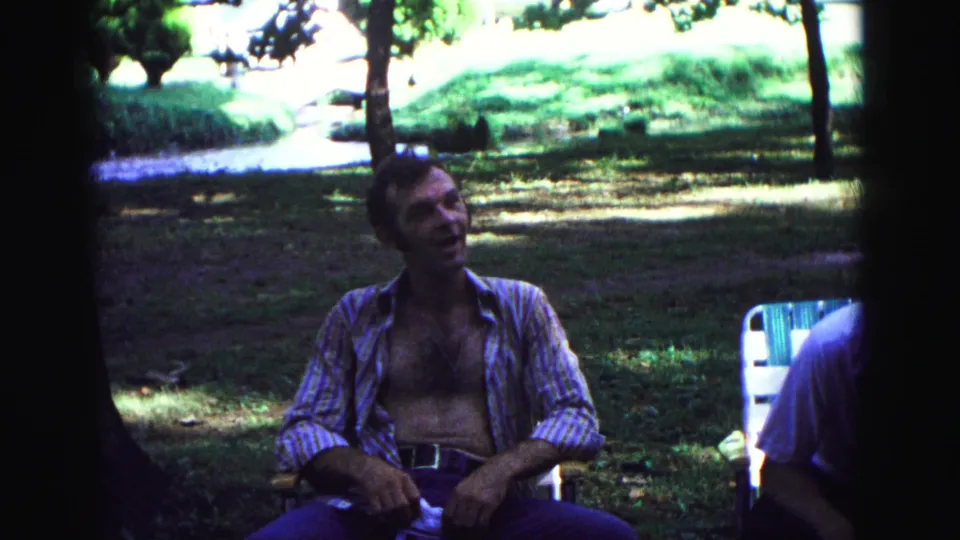 The Galena 1967 home movie shows the seated man mid-conversation in a shaded outdoor picnic setting.
