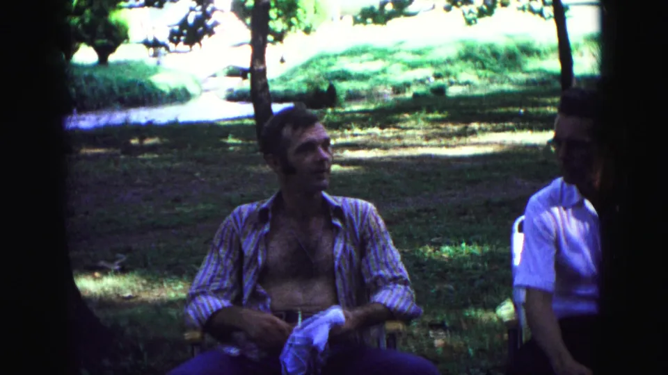 At the end of the 1967 Galena picnic clip, the seated man holds a cloth while turning toward another adult.